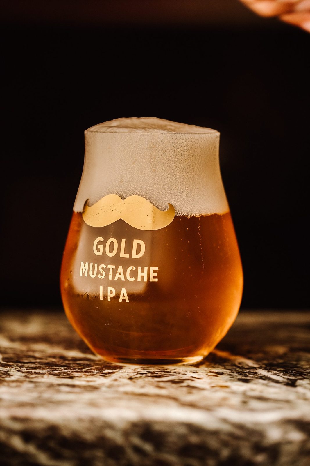Un verre tulipe rempli de Gold Mustache IPA, mousse épaisse, doré à la lumière