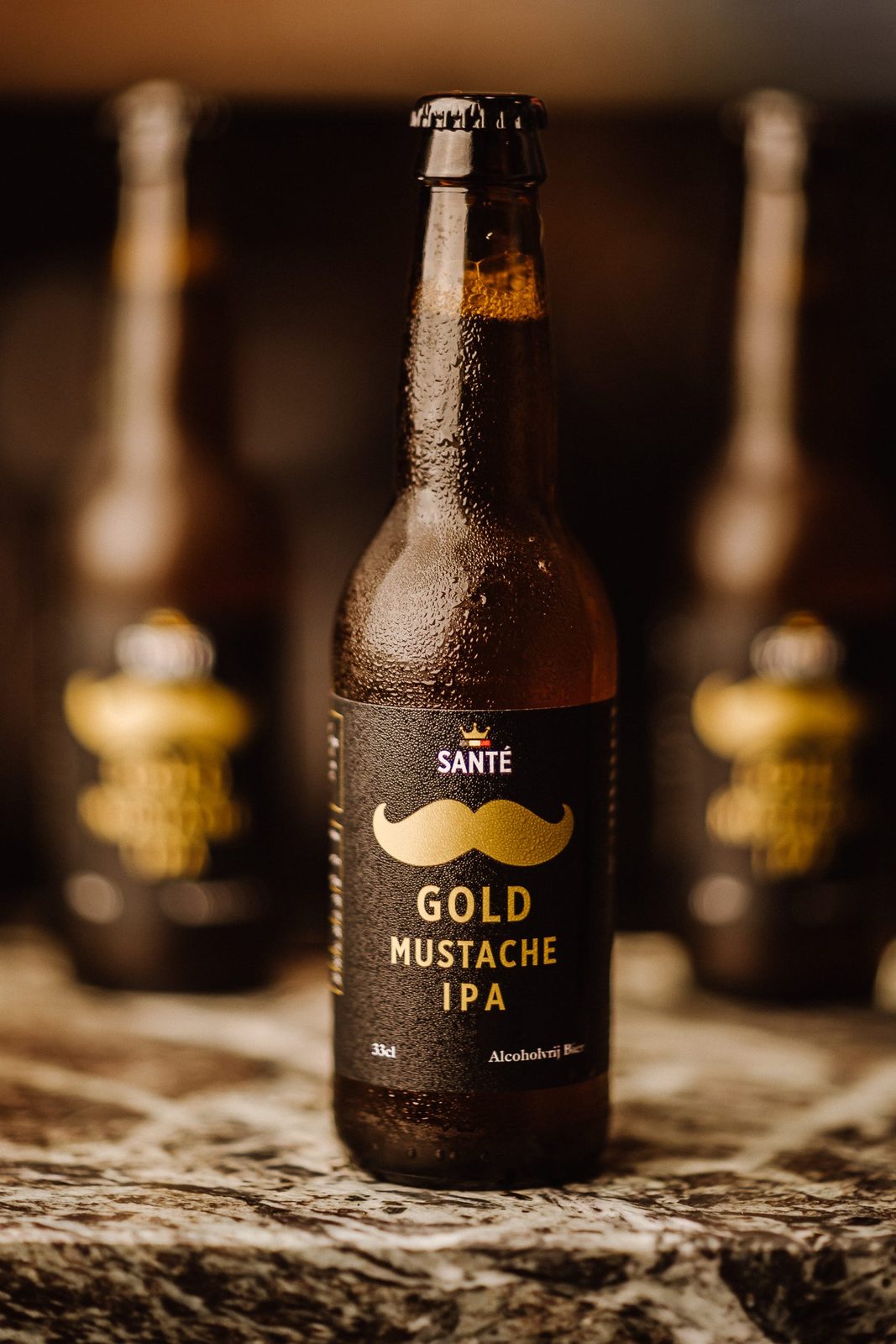 A chilled bottle of Gold Mustache IPA 0,3% on a marble bar top, more bottles out of focus behind it