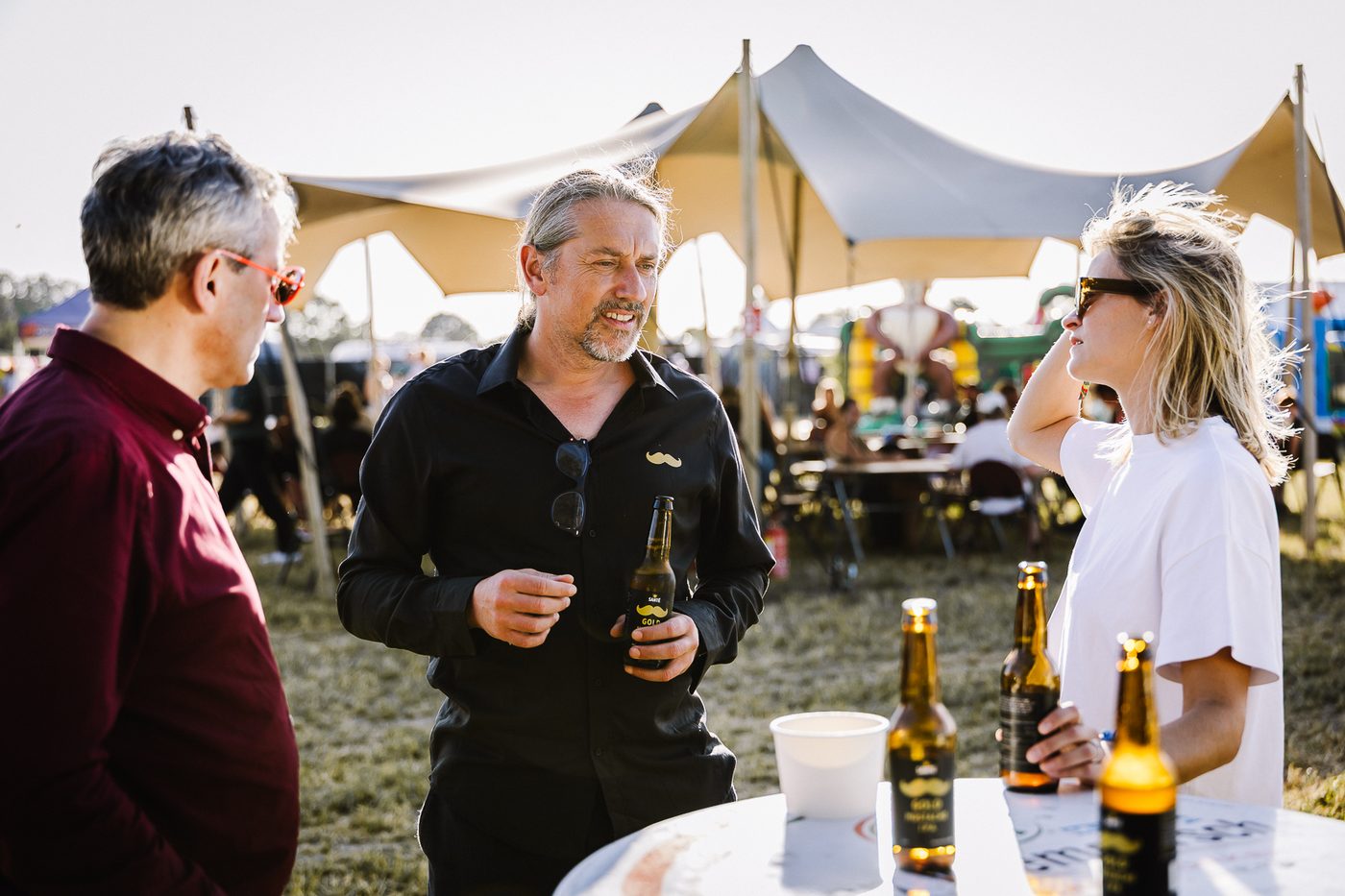 Friends standing and talking with bottles of Gold Mustache at an outdoor festival