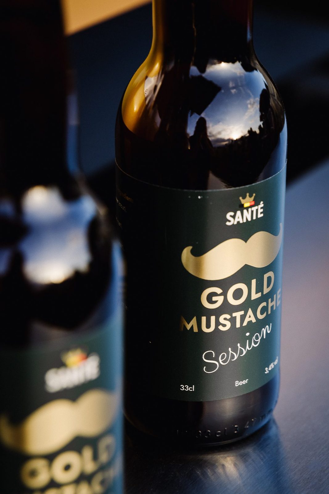 Twee flessen Gold Mustache Session 3,4% naast elkaar, etiket en logo van dichtbij